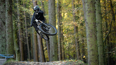 Radfahrer mit Fullface-Helm springt hoch mit einem Cube Stereo ONE77 Fully Mountainbike.