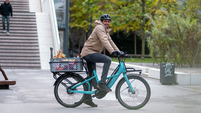Ein Radfahrer fährt mit seinem blauen Cube Longtail durch die Innenstadt. Er hat auf dem Gepäckträger eine Kiste mit Lebensmitteln gelagert.
