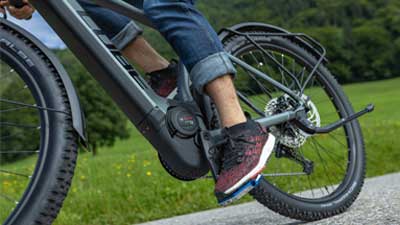 Abgebildet ist eine Nahaufnahme eines grauen Cube Reaction Hybrid Allroad Bikes. Genauer betrachtet wird das Tretlager, sowie der Motorblock des E-Bikes während der Fahrt.