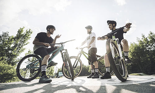 Drei Freestyle-Radfahrer stehen an ihren Fahrrädern und unterhalten sich an einem sonnigen Tag.