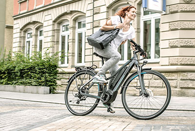 Eine Frau fährt mit einer Handtasche unter dem Arm durch die Innenstadt, mit einem Winora Fahrrad.