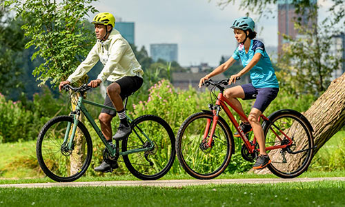 Radfahrer und Radfahrerin fahren auf Crossrädern an einem Park entlang.