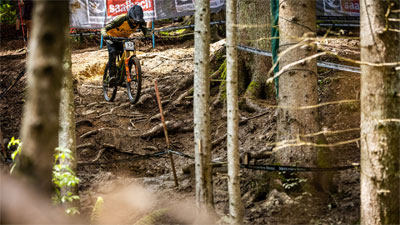 Ein Downhill Rennfahrer fährt einen verwurzelten Abhang herunter.
