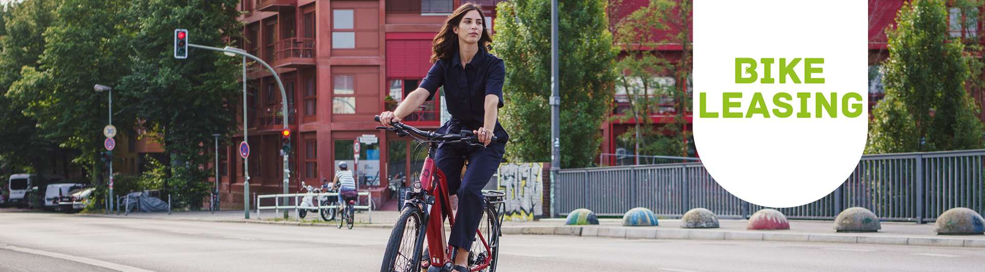 Eine Frau fährt in der Stadt mit einem rotem E-Bike über die Straße. Neben ihr ist das Bikeleasing-Logo zu sehen.