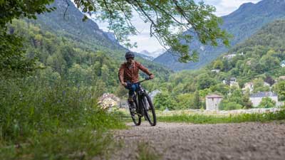 Ein Radfahrer fährt mit seinem Mountainbike über einen Schotterweg, im Hintergrund ist eine bergige Landschaft.