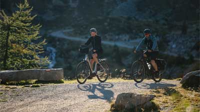 Ein Paar fährt mit dem Mountainbike auf einem Radweg, im Hintergrund ist bergige Landschaft.