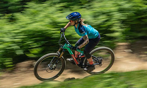 Zu sehen ist eine Frau auf einem Mountainbike, welche schnell über einen Waldweg fährt. 