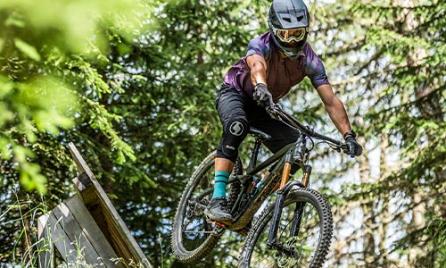 Radfahrer mit Fullface-Helm fährt auf einem Fully-Mountainbike durch den Wald.
