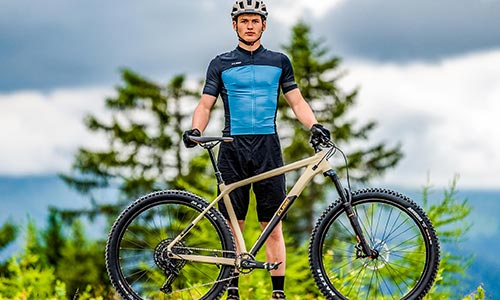 Mann in Fahrradbekleidung steht hinter einem Mountainbike Hardtail.