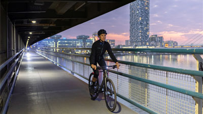 Zu sehen ist eine Frau auf ihrem Fahrrad, sie fährt durch eine Unterführung, im Hintergrund ist eine Großstadt zusehen.