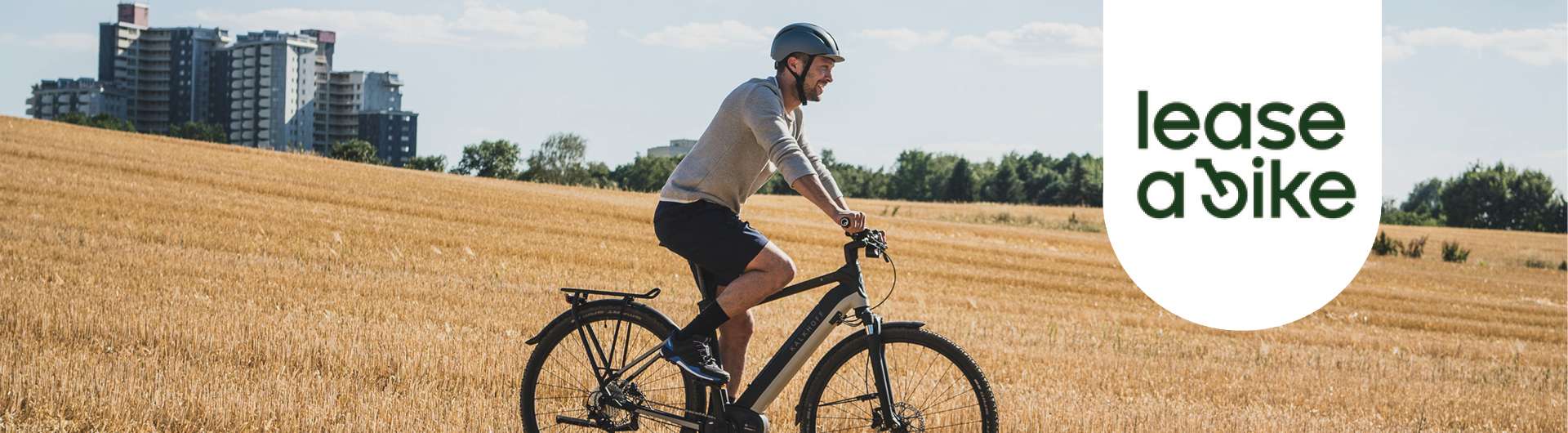Ein Mann fährt auf seinem schwarzen E-Bike. Im Hintergrund ist ein Weizenfeld zu sehen. Rechts von ihm ist das leas a bike logo zu sehen.